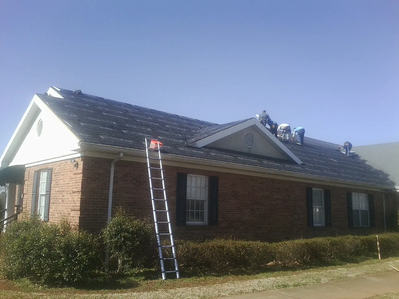 Crew tearing shingles off a brick ranch roof with a ladder set — Metal Roof Repair work by our crew in Providence