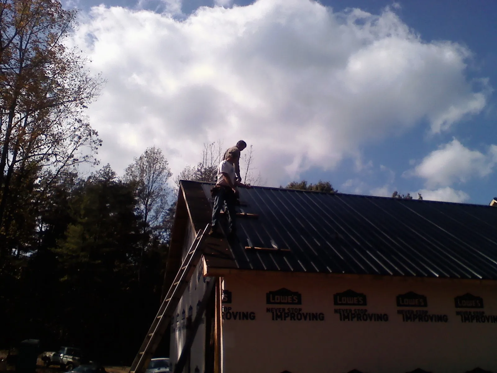Roofer fastening dark metal panels high against a cloudy sky, from a Roof Inspection job in Providence